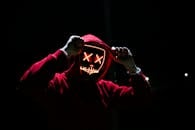 Home A spooky illuminated mask figure with a red hoodie in a dark setting, perfect for Halloween themes.