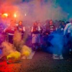 A lively group celebrating at night with color smoke bombs in a street festival.